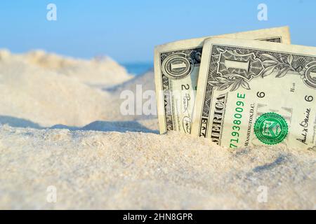 Zwei alte Dollarscheine im Sand auf dem Hintergrund des blauen Himmels am sonnigen Sommer Stockfoto