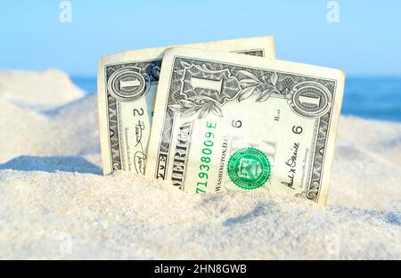 Zwei alte Dollarscheine im Sand auf dem Hintergrund des blauen Himmels am sonnigen Sommer Stockfoto