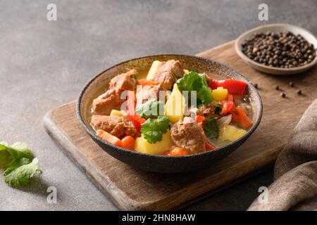 Rindereintopf mit Gemüse, Kartoffeln, Pfeffer, Karotten in einer Schüssel auf braunem Hintergrund. Europäische Küche. Nahaufnahme. Stockfoto