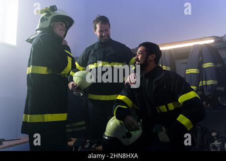 Glückliche Feuerwehrmänner Männer und Frauen, die sich nach dem Einsatz in der Feuerwehr unterhalten Stockfoto