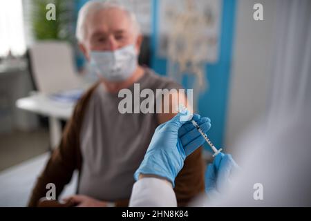 Nahaufnahme eines Arztes, der die Impfspritze Covid-19 hält und sich vorbereitet, sie an einen älteren Mann zu geben. Stockfoto