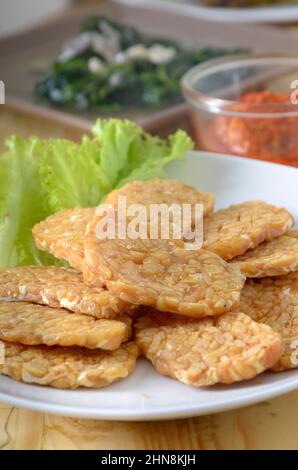 Gebratener Tempe/Tempeh auf weißem Teller, mit Eisbergsalat als Garnierung. Tempe, asiatische Lebensmittel aus Sojabohnen Stockfoto