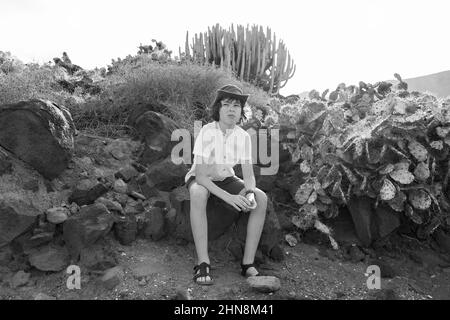 Porträt eines Teenagers in einem Poloshirt und einem Hut vor dem Hintergrund von Kakteen. Schwarz und Weiß. Stockfoto