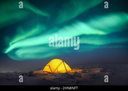 Gelbes Zelt von innen beleuchtet vor dem Hintergrund eines unglaublichen Sternenhimmels mit Aurora Borealis. Tolle Nachtlandschaft. Nordlichter im Winterfeld Stockfoto