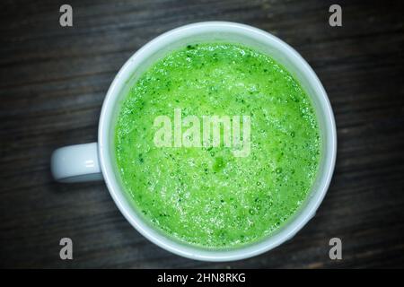 Weiße runde, breite Tasse mit frischer grüner Suppe auf dunklem Hintergrund. Isoliertes Objekt. Vegetarische Rohkost. Gemüsesmoothie. Vitamine und gesunde Ernährung Stockfoto