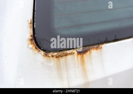 Rost auf der Seite des weißen alten Autos. Rostloch auf alter, abgenutzter lackierter Metalloberfläche. Stockfoto