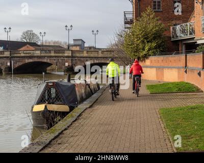 Allgemeiner Blick auf den Fluss Nene bei Southbridge, Northampton, Großbritannien, an einem sonnigen Wintertag; Radfahrer, Frau zu Fuß und Schmalboot Stockfoto