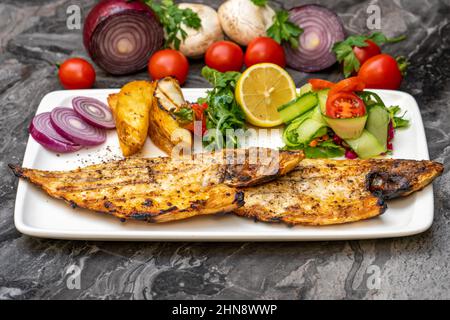 Gegrillte Seebrasse mit Salat und pommes auf dem dunklen Tisch Stockfoto