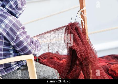Ein Arbeiter repariert und näht ein Fischernetz in der Nähe des Bootes. Das Konzept der Arbeit und manuelle Beschäftigung Stockfoto