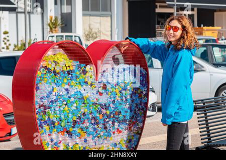 Das verantwortliche Mädchen übergibt den Kunststoff zum Recycling in einem herzförmigen Behälter, der von den Behörden auf der Straße der Stadt installiert wurde. Gewahrsein und die wahrnehmung Stockfoto