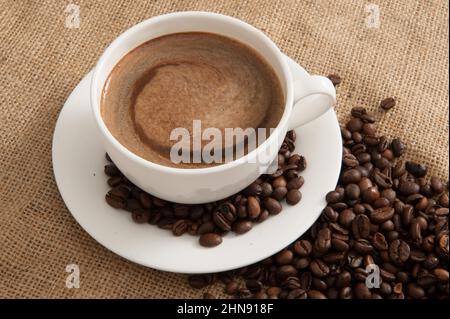 Tasse mit Kaffee und Kaffeebohnen und Dampf über Tasse auf Sackleinen Hintergrund Stockfoto