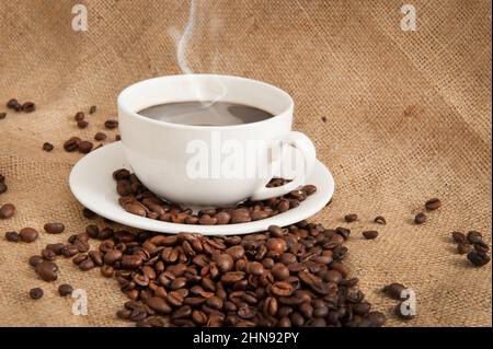 Tasse mit Kaffee und Kaffeebohnen und Dampf über Tasse auf Sackleinen Hintergrund Stockfoto