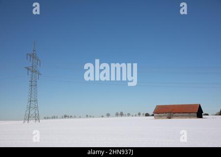 Pylon in der Nähe einer Holzscheune in einer winterlichen Landschaft in Süddeutschland Stockfoto
