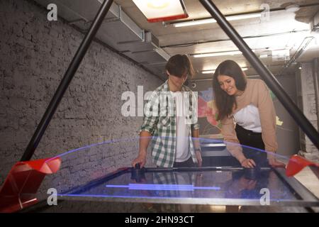 Glückliche junge Menschen lachen, spielen zusammen Air Hockey, kopieren Raum Stockfoto