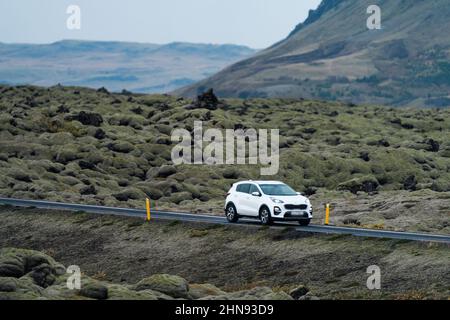 Weißes Auto, das durch riesige, von Moos bedeckte Lavafelder fährt Stockfoto