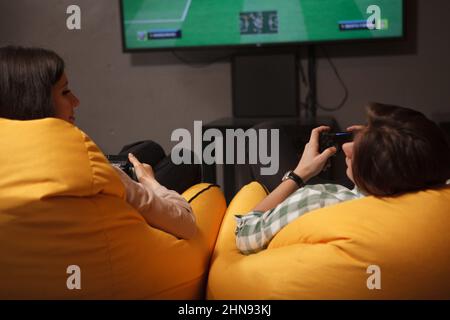 Junges Paar lächelt sich an, hält Gamepads, spielt Videospiele zusammen Stockfoto