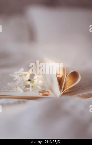 Goldener Ring und offenes Buch mit gefalteten Blättern in Herzform Stockfoto