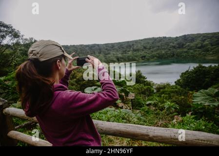 Junge Frau fotografiert Lake Botos, einen inaktiven Krater im Poas Volcano National Park, Costa Rica Stockfoto