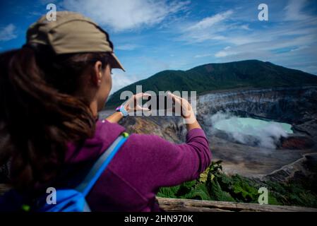 Junge Frau fotografiert den Vulkan Poas, einen aktiven 2.697 Meter langen Stratovulkan in Zentral-Costa Rica, der sich im Nationalpark des Vulkans Poas befindet Stockfoto