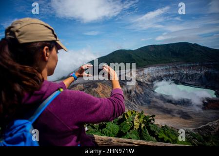 Junge Frau fotografiert den Vulkan Poas, einen aktiven 2.697 Meter langen Stratovulkan in Zentral-Costa Rica, der sich im Nationalpark des Vulkans Poas befindet Stockfoto