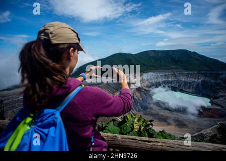 Junge Frau fotografiert den Vulkan Poas, einen aktiven 2.697 Meter langen Stratovulkan in Zentral-Costa Rica, der sich im Nationalpark des Vulkans Poas befindet Stockfoto