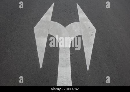 Verkehrsmarkierung 'Links- oder Rechtsabbiegen', weiße Umlenkpfeile auf grauem Asphalt, Konzept: Wichtige Entscheidung, ohne Alternativen, Wasserscheide, Kreuzung Stockfoto
