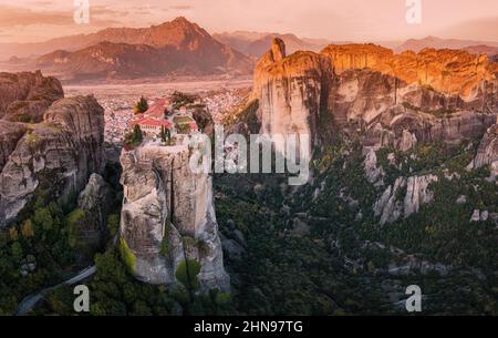 Panoramablick auf das Kloster der Heiligen Dreifaltigkeit in Meteora bei Sonnenaufgang und die Stadt Kalambaka in der Ferne. Tourist und Wallfahrt Erfahrung Stockfoto