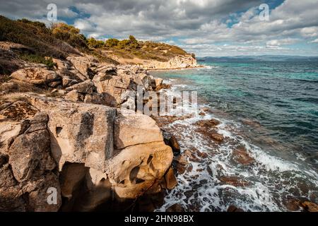 Blick auf die malerische Szene von Meereswellen, die auf die Felsen einer malerischen Insel in der Nähe des Ferienortes in der Region Chalkidiki krachen Stockfoto