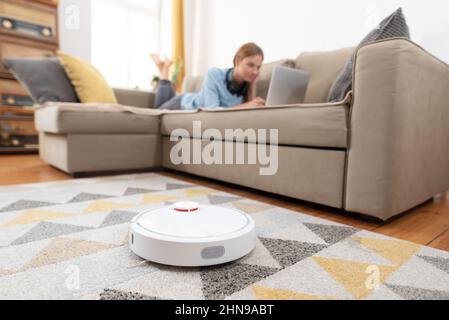 Moderner Roboter-Staubsauger. Autonomer Roboter reinigt die Wohnung, junge Frau hat Freizeit Stockfoto