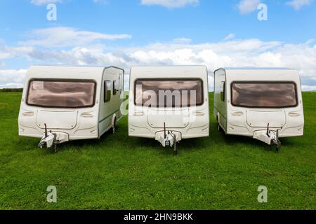 Wohnwagen-Anhänger, die zum Campen im Freien verwendet werden und auf einem grünen Rasen auf dem Parkgelände stehen, wo eine Familie einen unterhaltsamen Urlaub in t genießen kann Stockfoto