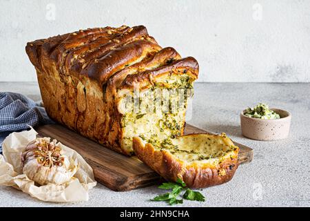 Hausgemachtes frisches Pull-Apart-Brot mit Kräutern (Petersilie, Thymian, Rosmarin, Dill), Knoblauch, Käse und würzige Butter auf einem Holzbrett. Stockfoto