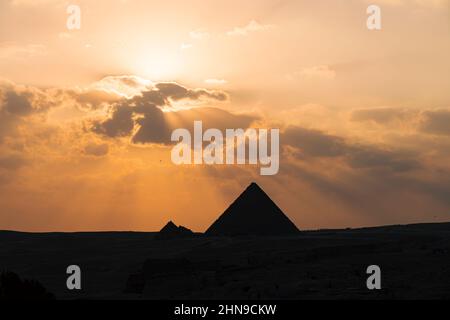 Der archäologische Komplex der Großen Ägyptischen Pyramiden befindet sich auf dem Hochplateau von Gizeh. Nachtlicht bei Sonnenuntergang. Die Sonne geht hinter der Pyramide unter. Stockfoto