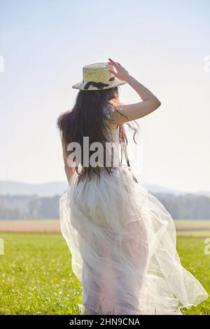 Junge schöne lange schwarze Haare asiatische Frau trägt ein lila romantisches Kleid stehen in einem hinterleuchteten Grasfeld Stockfoto