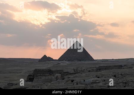 Der archäologische Komplex der Großen Ägyptischen Pyramiden befindet sich auf dem Hochplateau von Gizeh. Nachtlicht bei Sonnenuntergang. Die Sonne geht hinter der Pyramide unter. Stockfoto