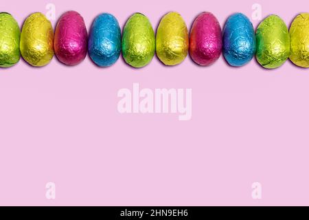 Ostereier in farbenfroher Folie auf rosa Hintergrund. Stockfoto