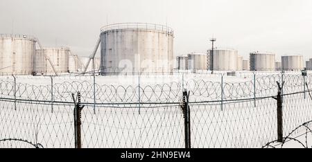Gasspeichertanks im Winter, Tanklager hinter einem Zaun mit Stacheldraht gekrönt Stockfoto