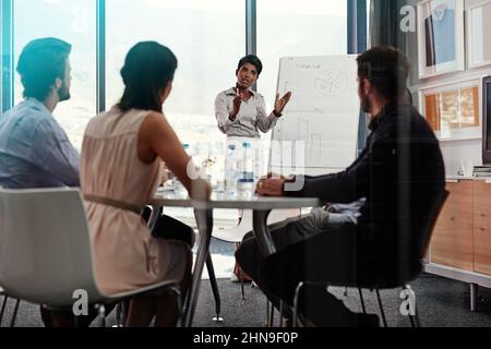 Erklären Sie ihren Plan im Detail. Aufnahme einer Geschäftsfrau, die eine Whiteboard-Präsentation vor einer Gruppe von Kollegen in einem Sitzungssaal gehalten hat. Stockfoto