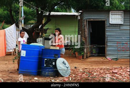 Zwei Frauen sammeln am Montag, den 14. Februar 2022, in Maracaibo, Venezuela, Wasser aus zwei Plastikfässern vor ihrem Haus aus Zing Sheets im Viertel La Pastora. Die Pandemie Covid-19 und die Brennstoffkrise haben die wirtschaftliche Situation verschärft, die dieses Land, das reich an Ölvorkommen ist, seit Jahren erlebt. Nach den Ergebnissen einer Studie der Katholischen Universität Andrés Bello (UCAB). Seit 2014 leidet das Land unter einem Mangel an grundlegenden Dienstleistungen wie Trinkwasser, Strom, Gas, Arbeitslosigkeit, Hyperinflation und den kontinuierlichen Abwertungen der lokalen c Stockfoto