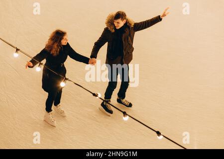 Ein junges Paar, das in Liebe skaten, Hände haltend und lächelnd, Draufsicht. Stockfoto