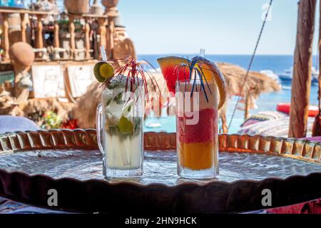 Frische Cocktails mit kalten Orangen und Himbeeren und Mojito am Tisch am Strand mit sonniges Meer. Eisgekühlte, bunte Getränke im Tropical Resort. Hotelurlaub Stockfoto