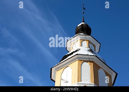 Ein gelber Uhrenturm einer alten Kirche mit blauem Himmel und weißer dünner Wolke auf einem Hintergrund Stockfoto