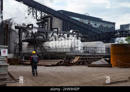 Temirtau, Kasachstan - 08. Juni 2012: Arcelor Mittal Hütte draußen. Wärmetauscher, Rohre und Förderbänder. Arbeiter links, verschwommen. Stockfoto