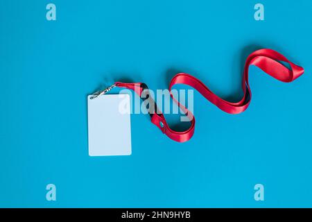 Weißes Plastikabzeichen, rote Lanyard mit leerem Raum, isoliert auf blauem Hintergrund Stockfoto