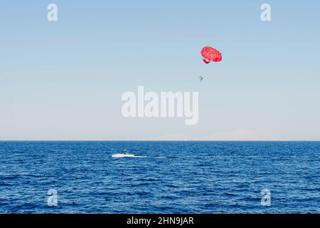 Sportliche Aktivitäten - Parasailing über dem Mittelmeer. Ein Schnellboot zieht mit einem Touristen einen gelben Fallschirm. Extreme Unterhaltung für Touristen auf Th Stockfoto
