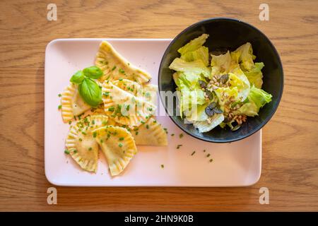 tiroler Knödel gefüllt mit Spinat, serviert mit Schnittlauch, Basilikumblättern und grünem Salat in einer Schüssel Stockfoto