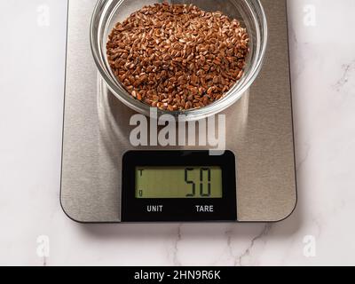 Rohe Leinsamen in einer Glasschale auf digitaler Küchenwaage. 50g Leinsamen auf der Waage, die Gramm anzeigt. Elektronisches Haushaltsmessgerät. Stockfoto