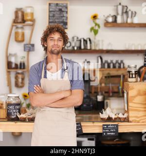Immer ein freundliches Gesicht im Café. Porträt eines Baristas, der fröhlich an einem Café-Tresen steht. Stockfoto