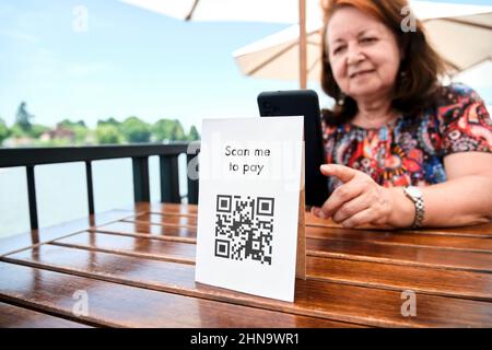 Reife hispanische Frau scannt mit ihrem Smartphone einen QR-Code, um ihre Restaurantrechnung mit kontaktloser, bargeldloser Technologie zu bezahlen. Konzentrieren Sie sich auf den Code. Stockfoto