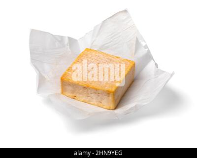 Einzelnes ganzes Stück Limburger oder Herve Käse mit starkem Geruch auf Packpapier isoliert auf weißem Hintergrund Stockfoto