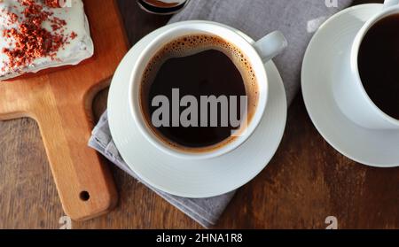 Roter Samtkuchen und zwei Kaffeetassen zum Frühstück auf Holzhintergrund. Leckeres Dessert. Nahaufnahme Stockfoto